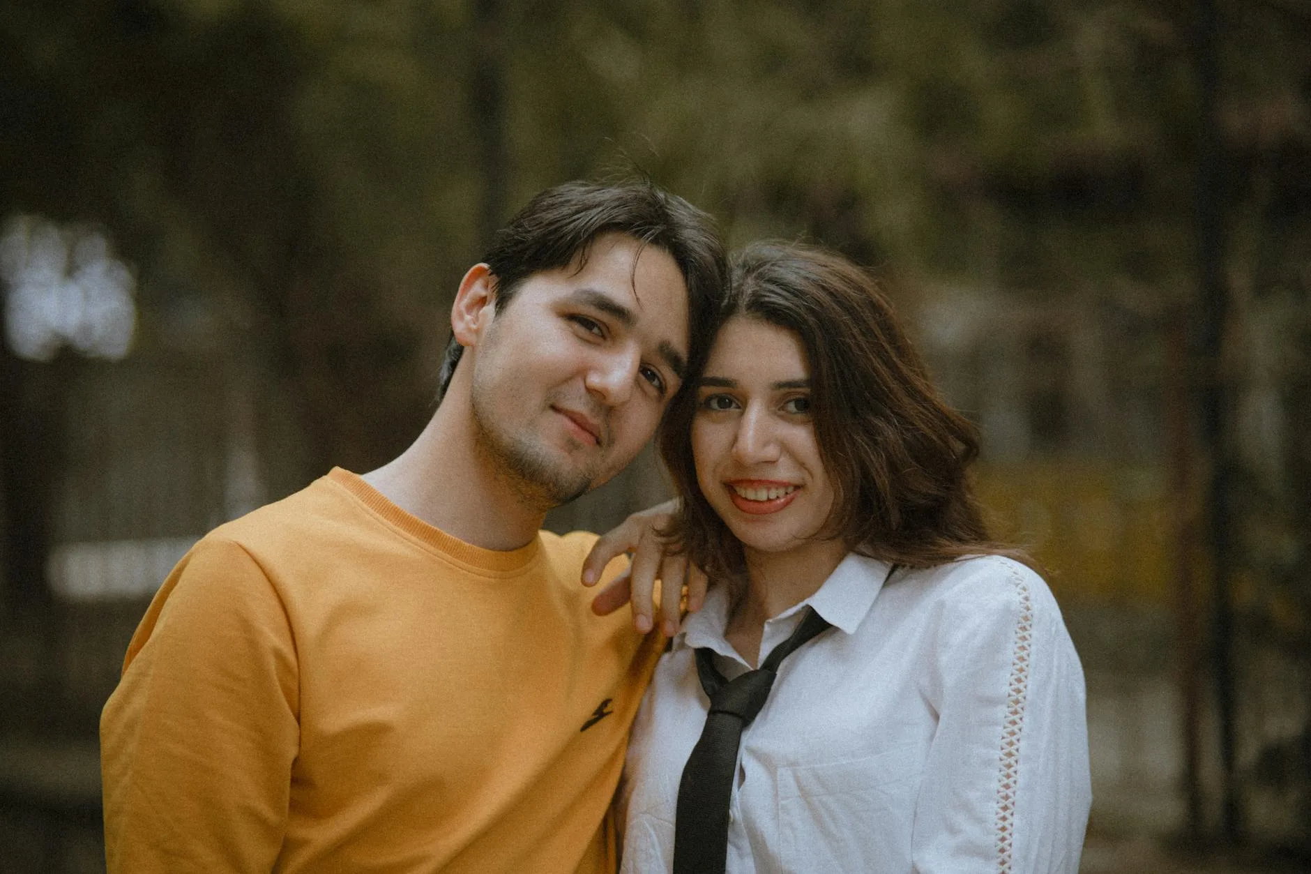 Charming couple posing outdoors in relaxed, casual clothing, displaying joyful expressions.