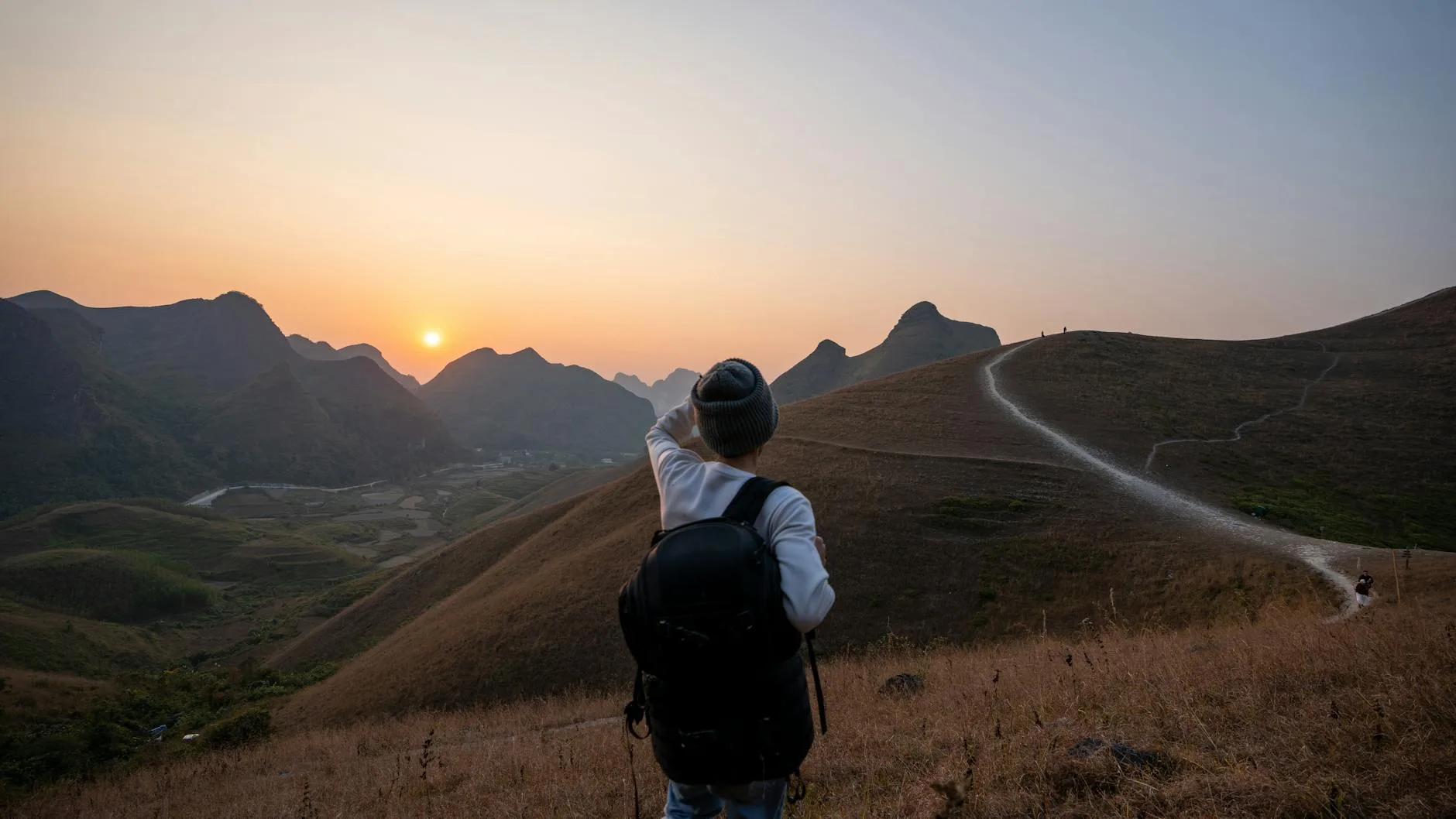 Back view of a hiker pointing at a breathtaking sunset over the mountains.