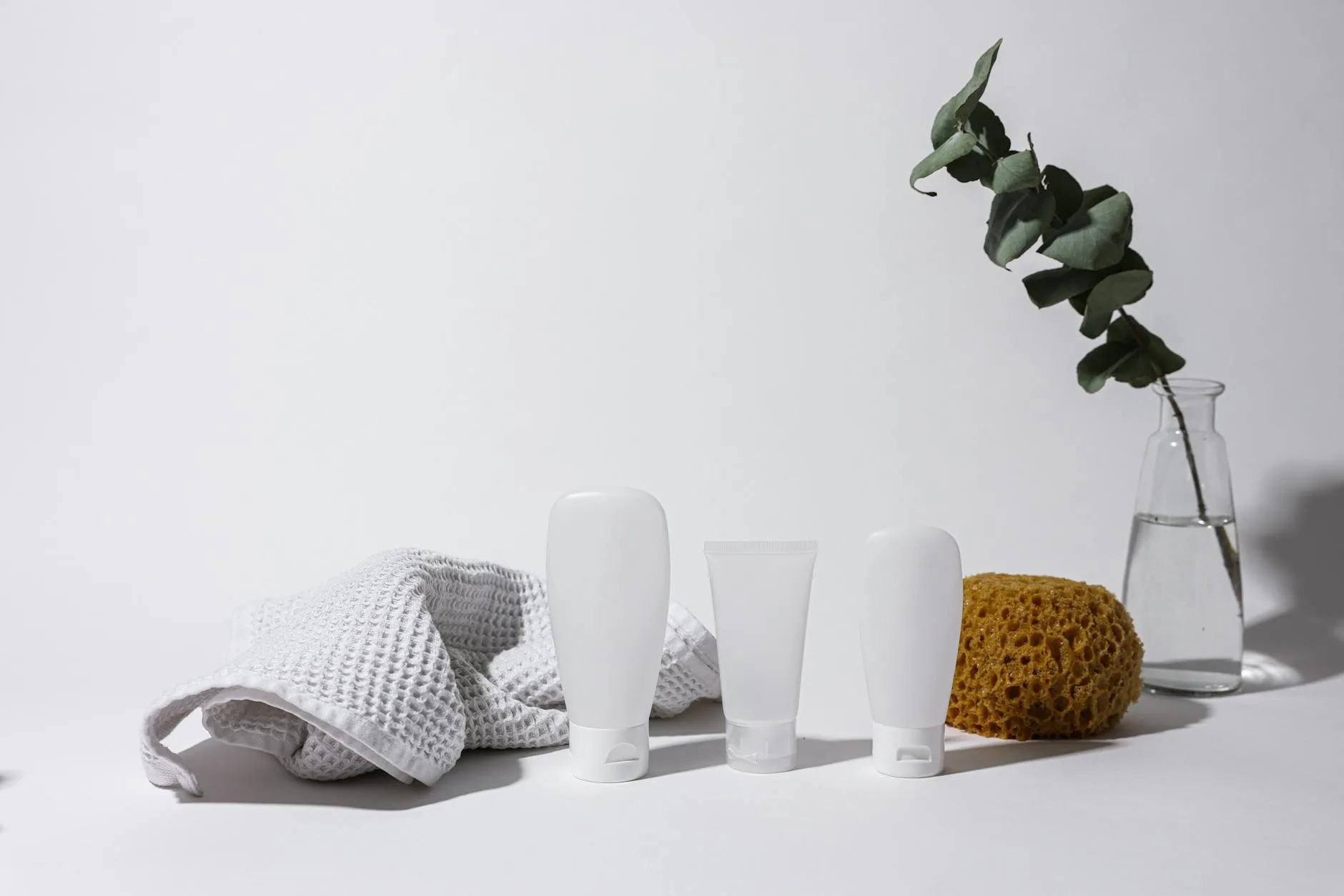 Simple and clean spa arrangement with white bottles, towel, and eucalyptus in vase.