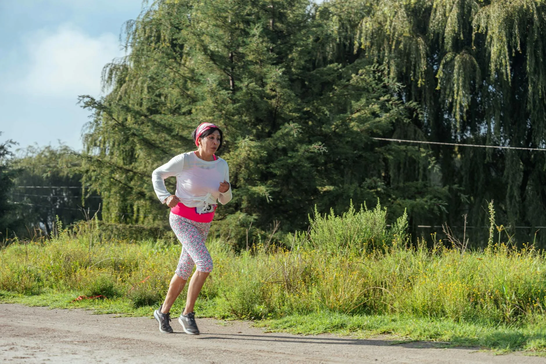 Woman jogging along a forest path under the bright sun, embracing nature and fitness.