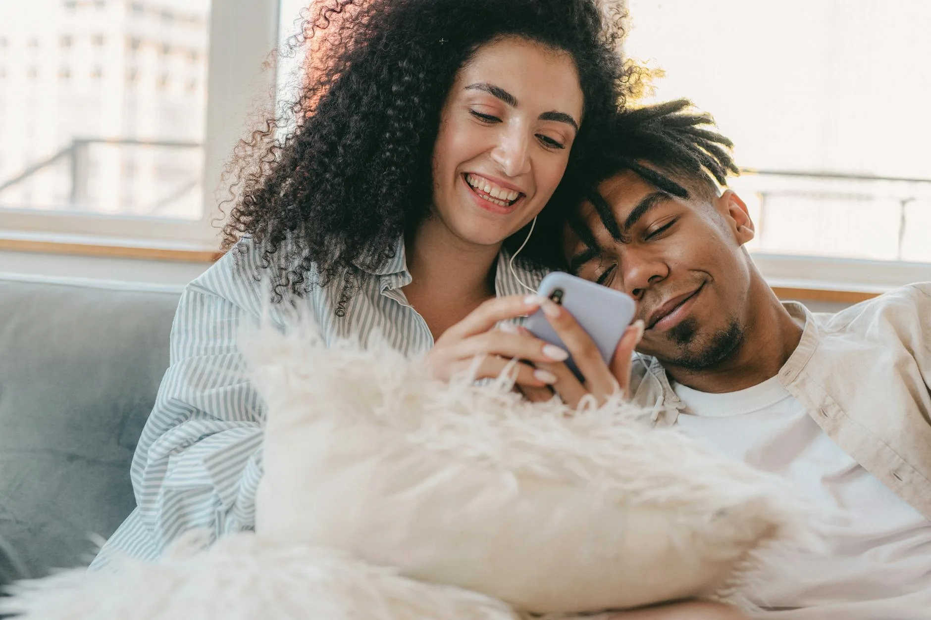 Interracial couple enjoying a cozy moment together with a smartphone on the couch.