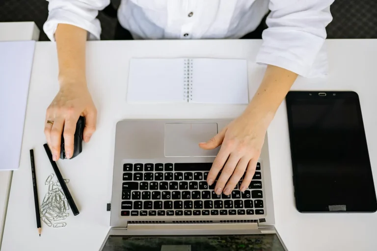 Top view of an office workspace with a laptop, tablet, and hands typing. Ideal for business and technology themes.