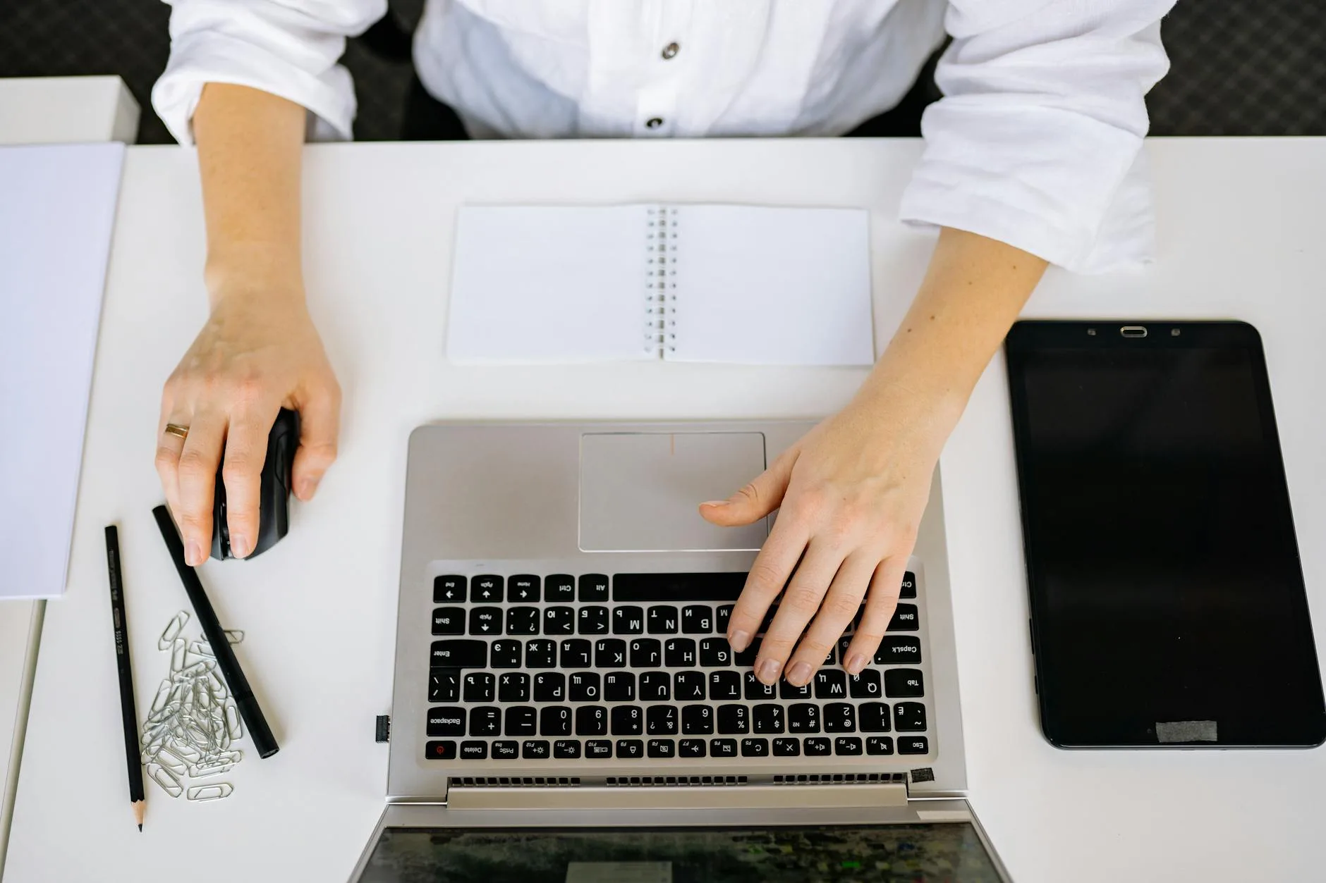 Top view of an office workspace with a laptop, tablet, and hands typing. Ideal for business and technology themes.