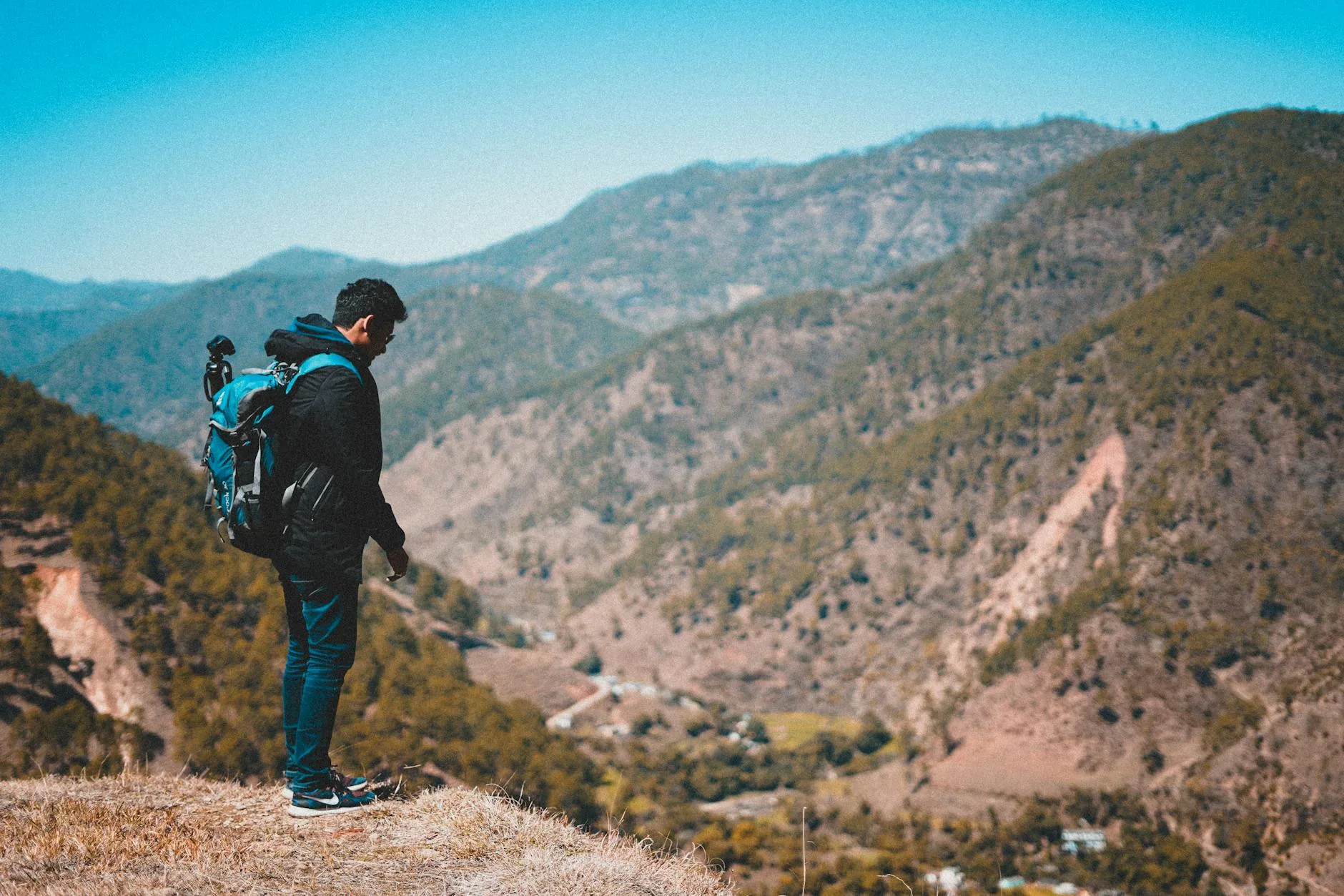 A man with a backpack standing on a hill overlooking a stunning mountain valley view.